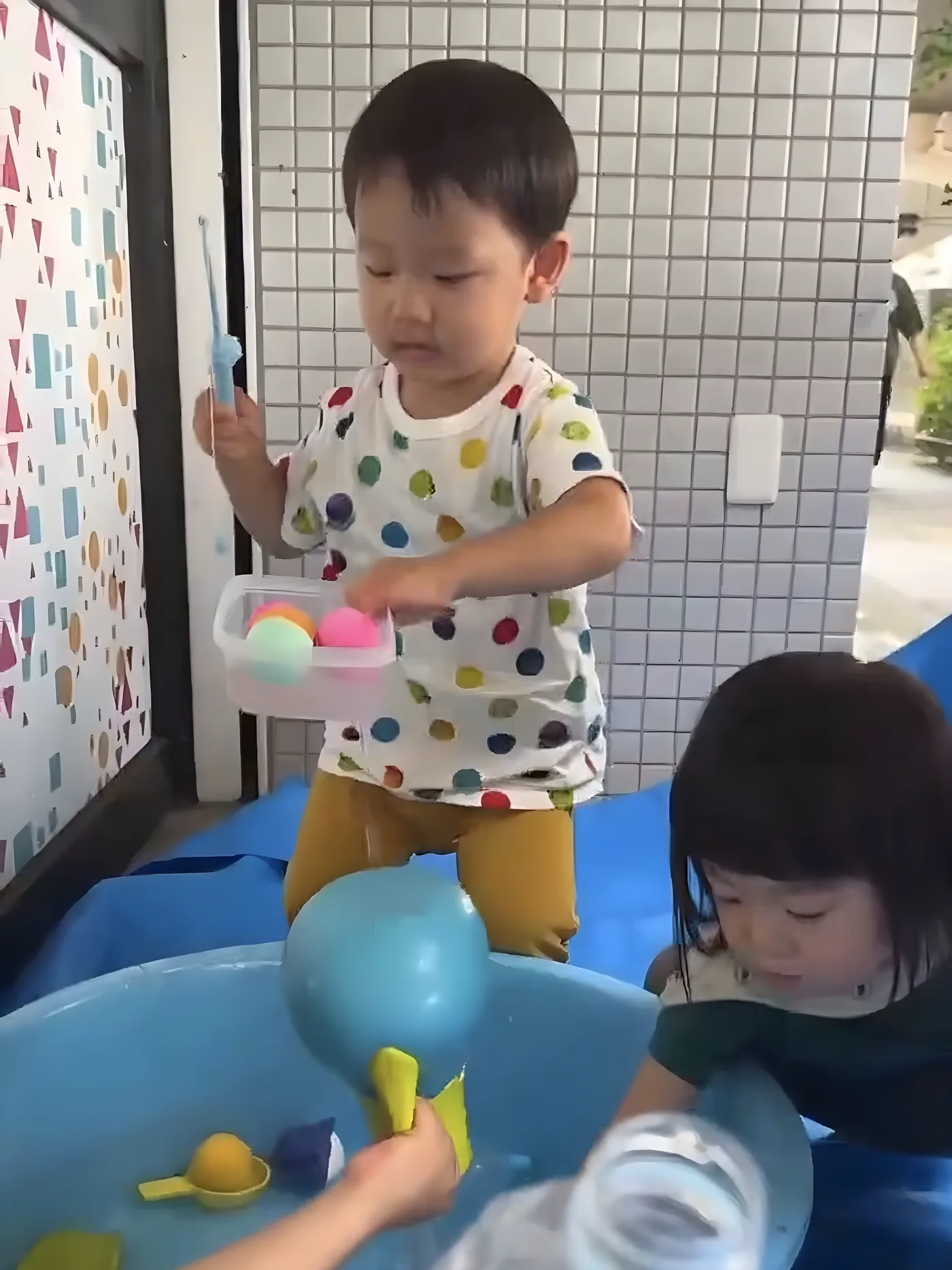 タライのそばで水あそびに夢中になっている子ども