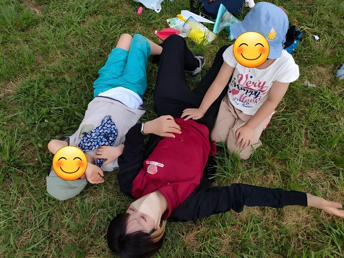 公園の芝生で職員と子どもたちが遊ぶ様子(お顔はスタンプで隠しています)